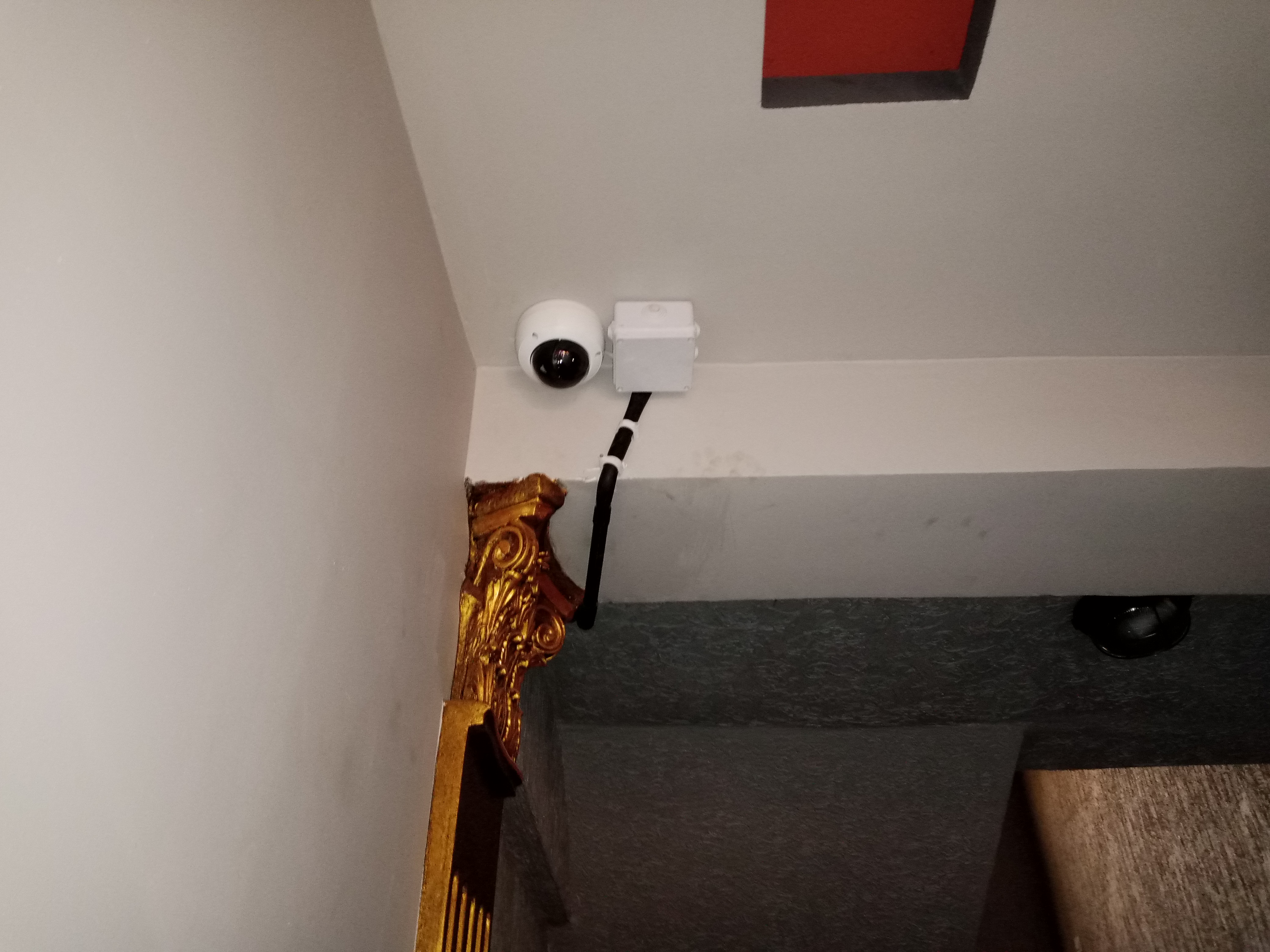 A dome CCTV camera mounted on indoor ceiling with adapter box next it