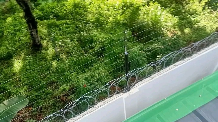 An electric fence on top of a razor wire which is on top of a wall fence